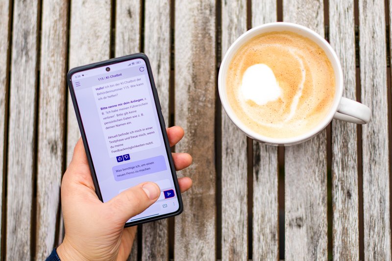 Ansicht einer Hand, die ein Handy mit dem 115-Chatbot auf dem Bildschirm hält.