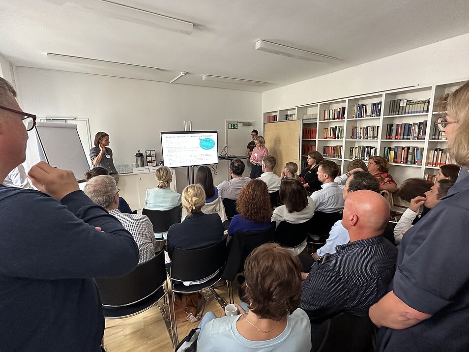 Fotografie eines Workshops mit vielen Menschen, die einer Referentin lauschen