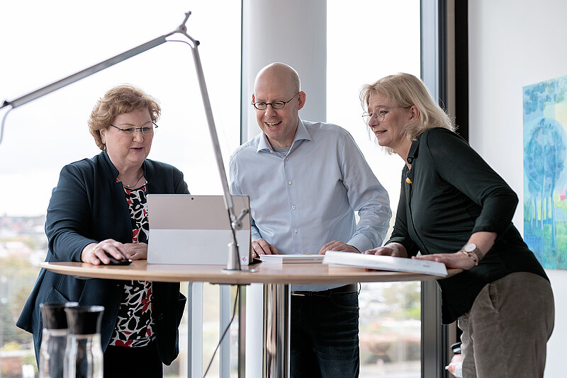 3 Personen beugen sich über einen Laptop