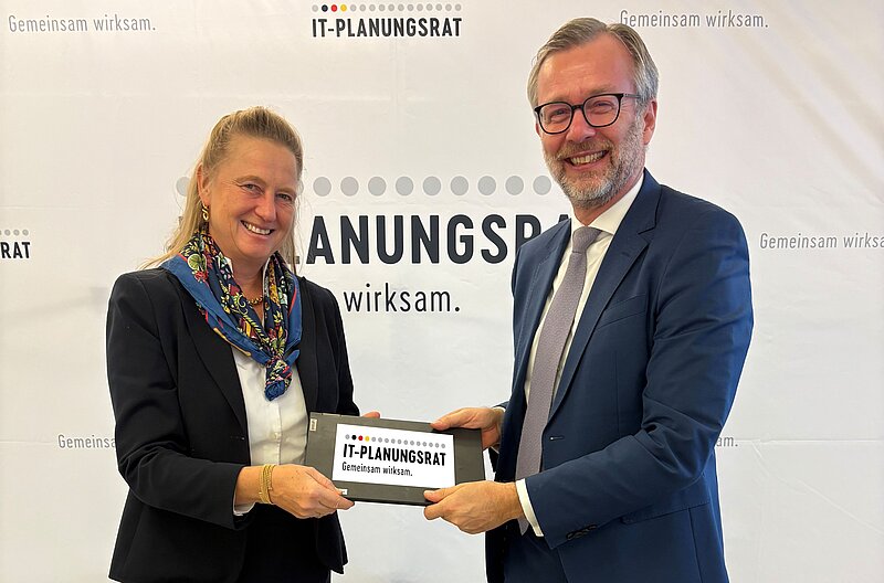 Foto von Dr. Geue und Prof. Dr. Hölscher, die beide ein iPad mit dem eingeblendeten Logo des IT-Planugnsrats in den Händen halten
